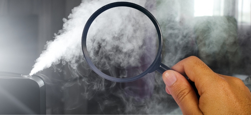 Man's hand holding magnifying glass pointing it on the smoke from humidifier