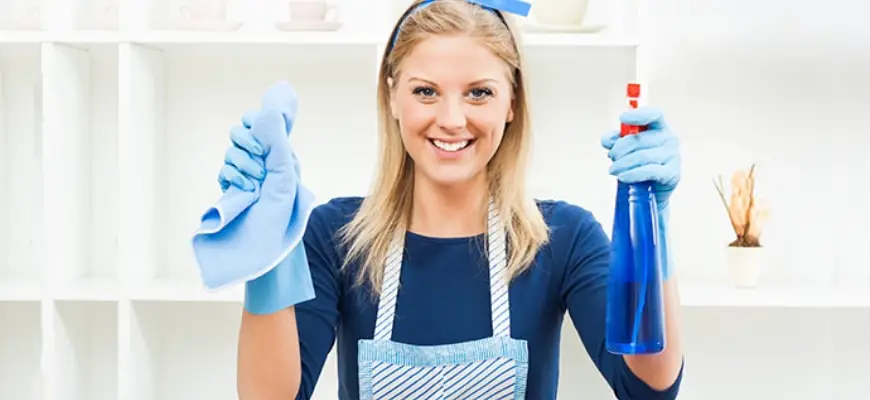 Woman smiling holding spray cleaner and cloth in white cabinet background