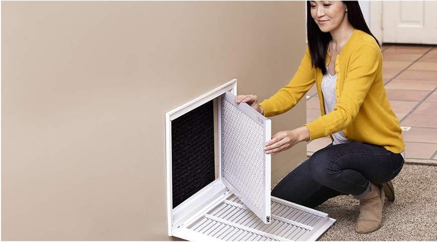 Woman in yellow jacket opening the furnace filter on the wall