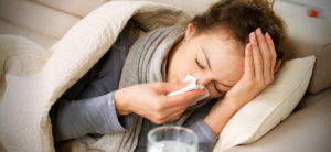 Woman sick, blowing her nose while lying on the bed