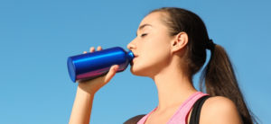 Woman drinking water from blue bottle in sky blue background